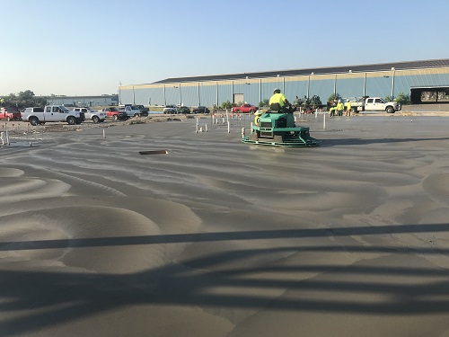 Freshly poured concrete slab with person smoothing it our with a large machine