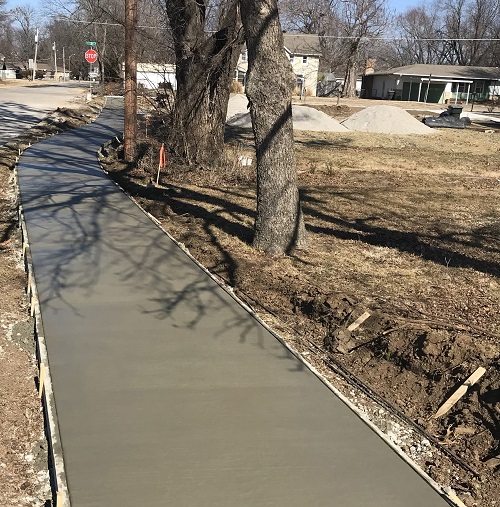 Freshly poured sidewalk winding down a road.